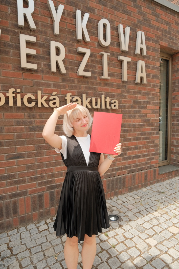 Anna holding her graduation folder outside Masaryk University in Brno